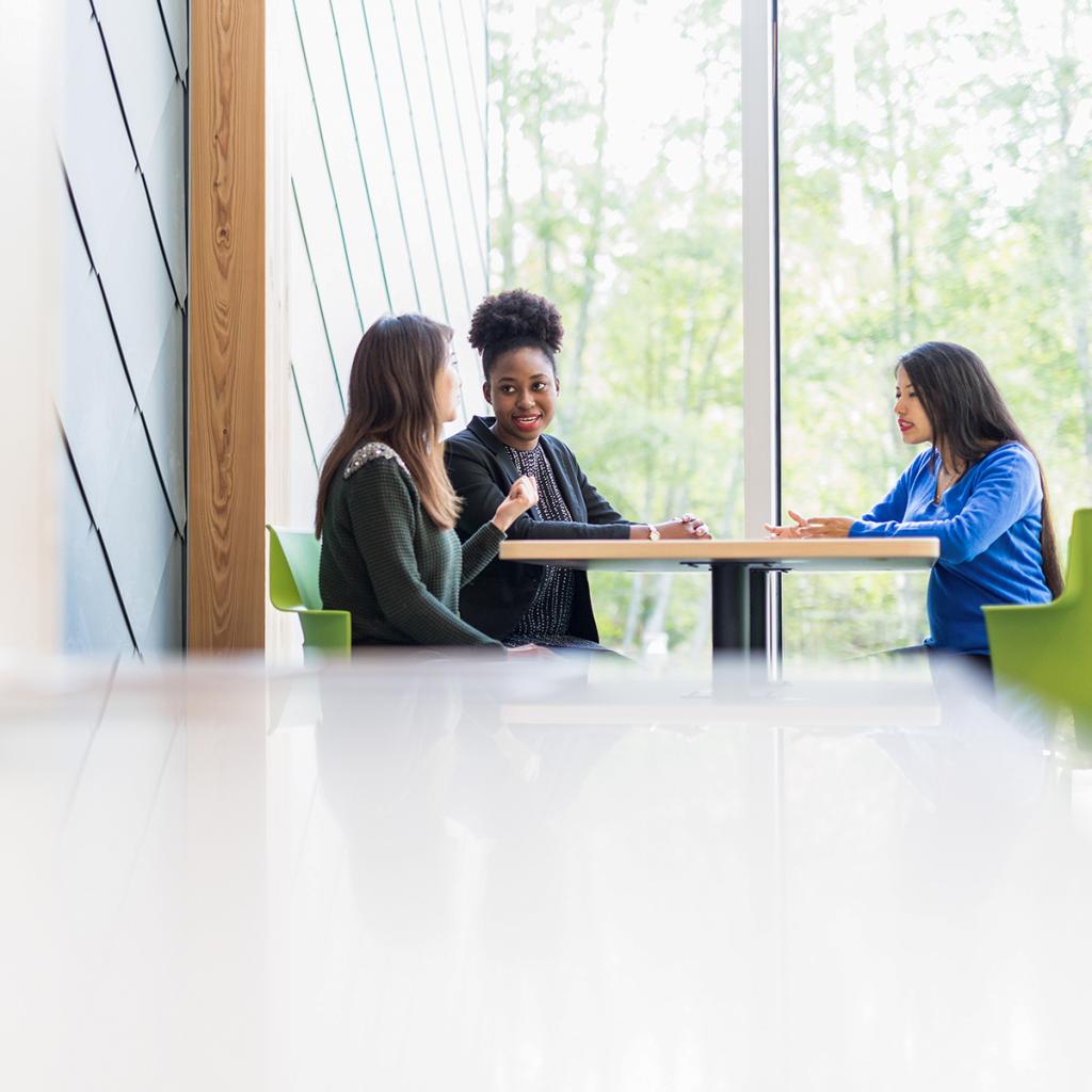 three-students-sitting-at-table-by-sunny-window