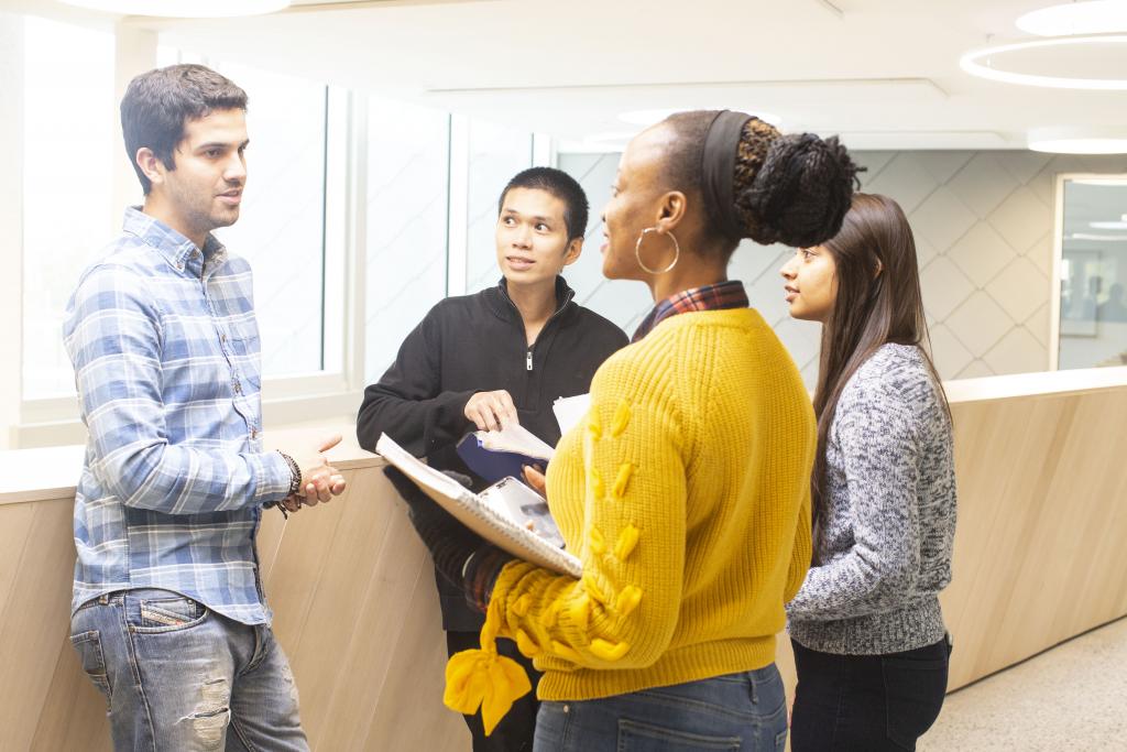 Group-of-four-students-standing-and-talking-with-books-in-hand