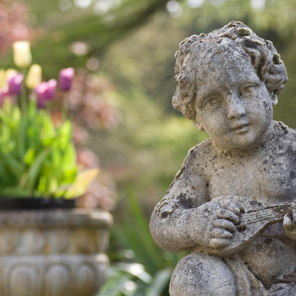 Stone statue of a cherub playing a mandolin and flowers in the university garden.