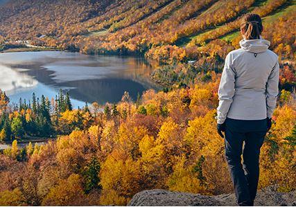A person in a grey jacket stands overlooking a river and fall-coloured trees.
