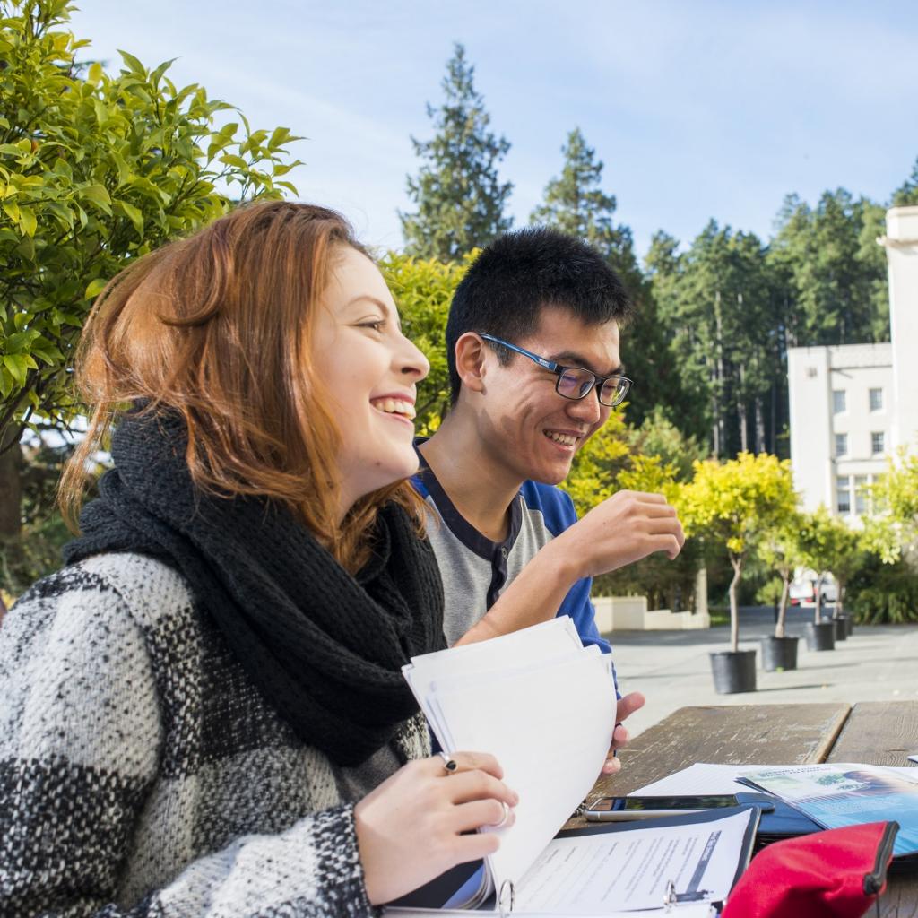 Two students smile and look over papers at a picnic table at RRU