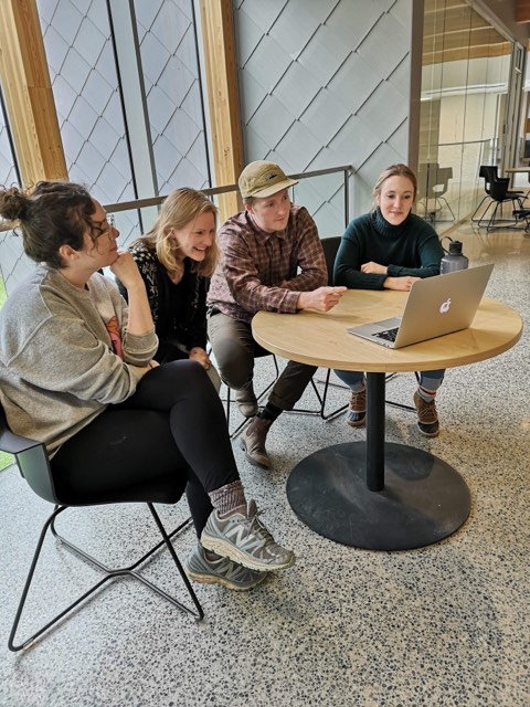 Four-students-sitting-together-at-table-looking-at-laptop