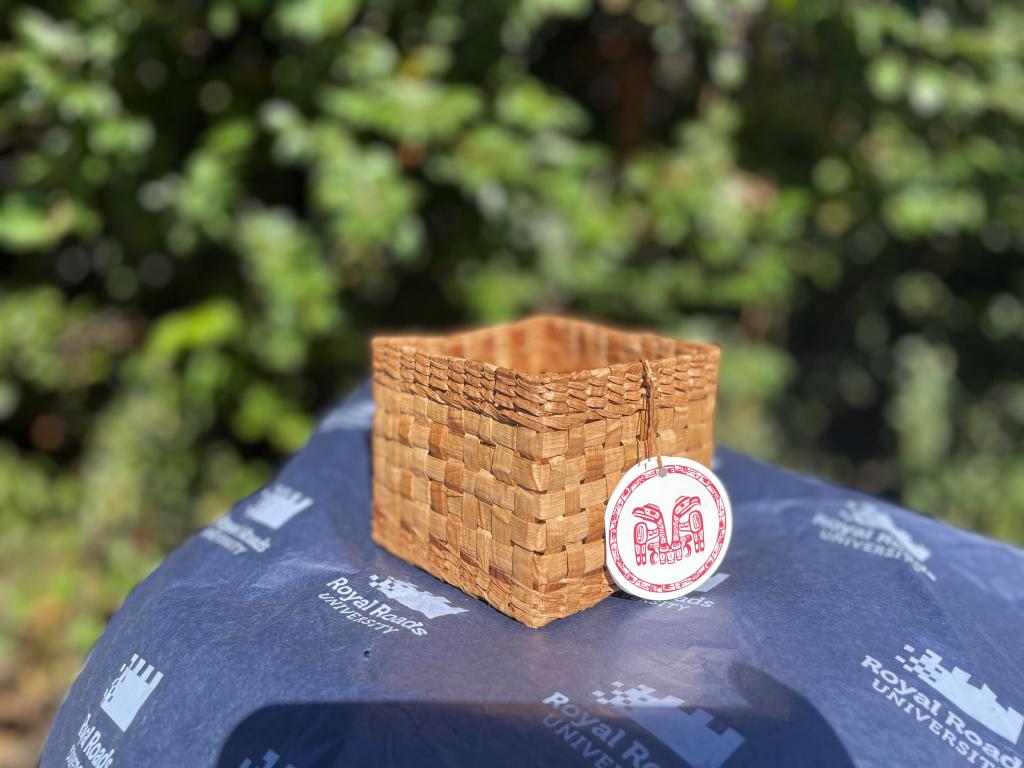 A woven basket sits on a table, covered in a blue Royal Roads-branded table cloth.