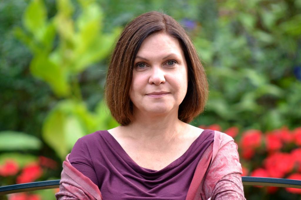 Associate faculty member Tabea Berg poses for a head-and-shoulders portrait with blurred out greenery behind her.