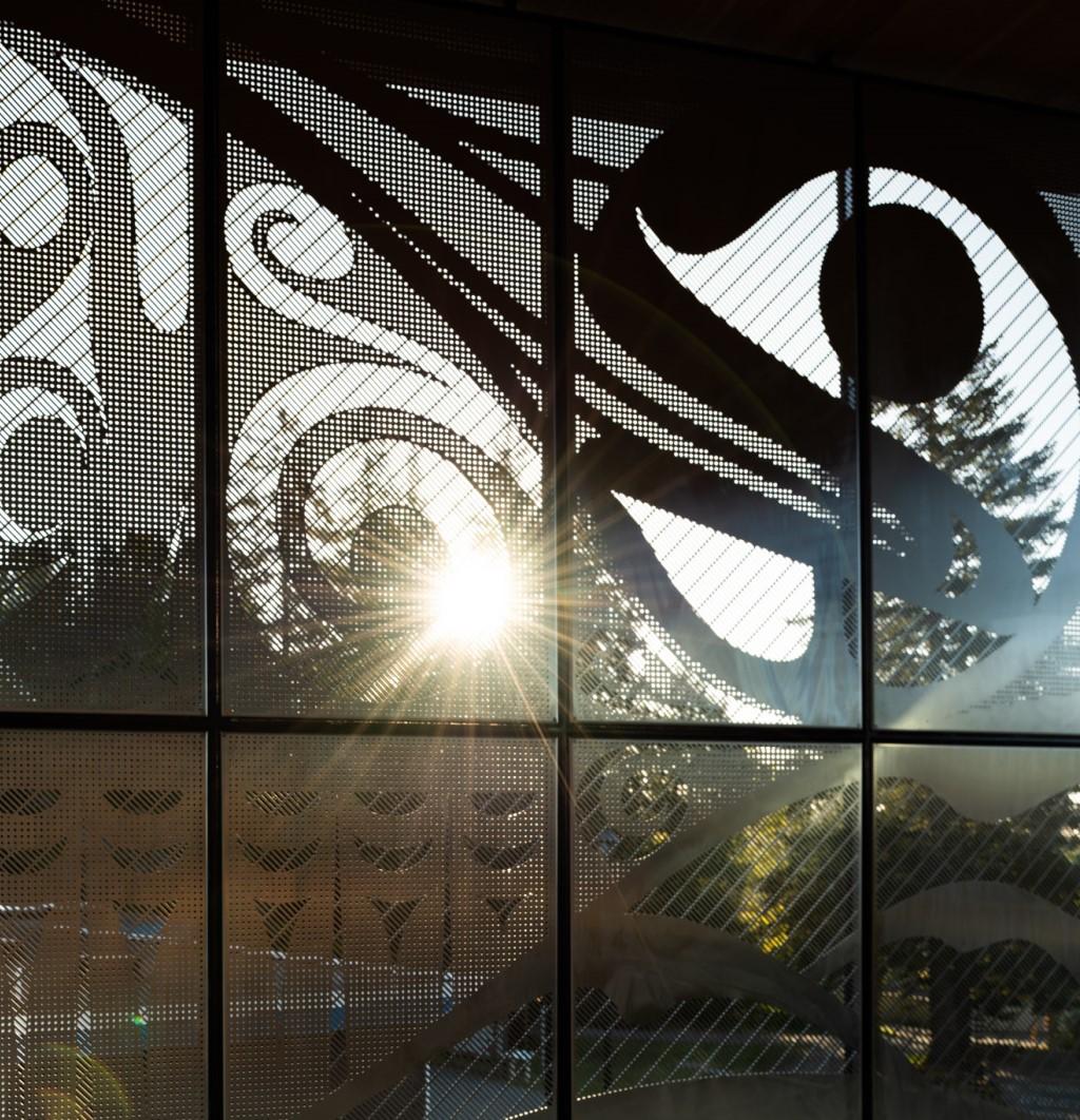Sun shines through metal artwork designed by Kwakwak’awakw artist Carey Newman in the Dogwood Auditorium entrance.