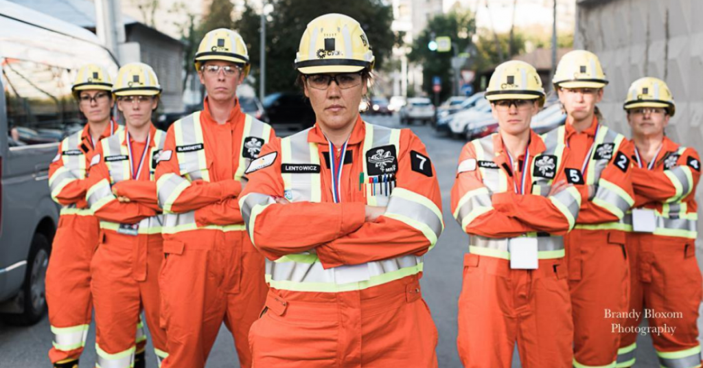 A group of women miners pose in orange overalls and helmets. 