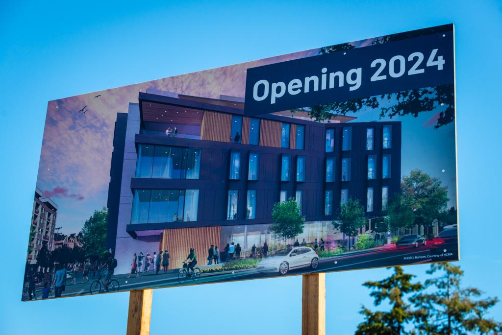 A giant sign against the blue sky with a rendering of the campus and the words "opening 2024."