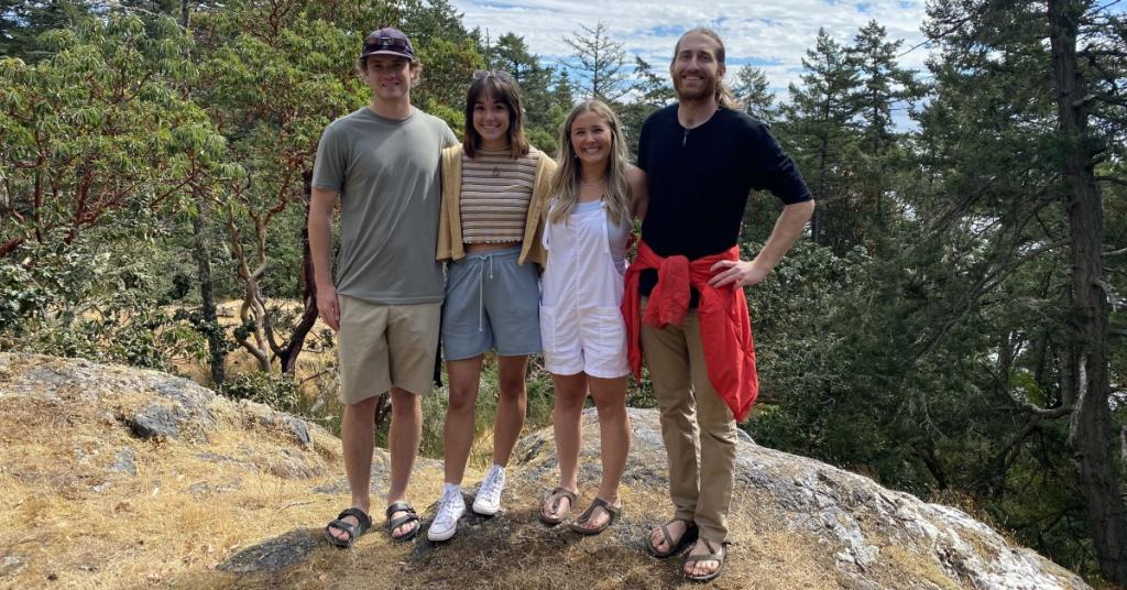 Jake Edwards, Hayley Houlden, Shannon Tallon and Caleb Gaeke stand atop a Garry Oak meadow that overlooks the trees and water.