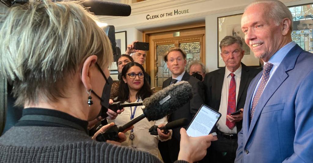 Journalists gather around former Premier of BC John Horgan inside the BC legislature. 