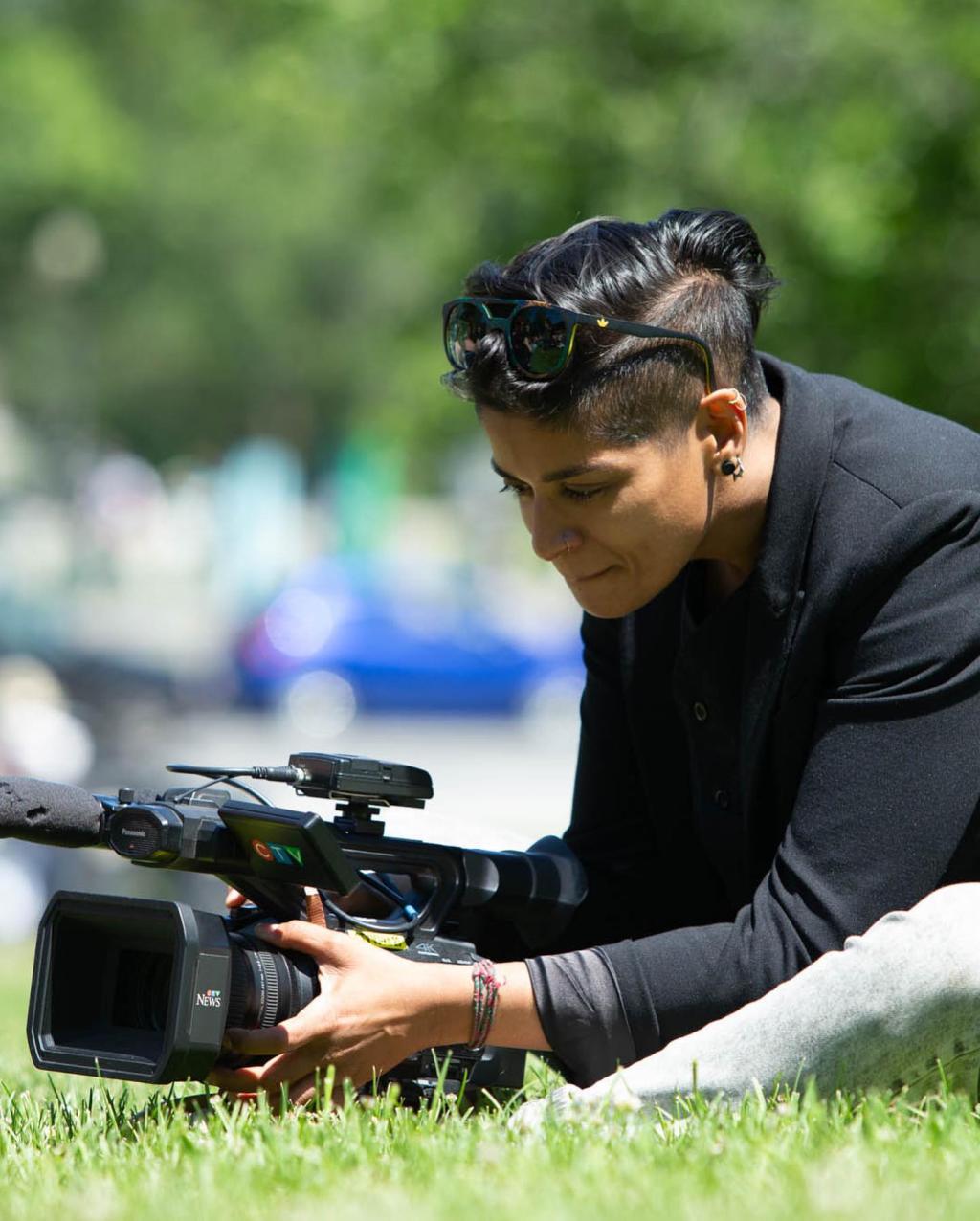 Iman Kassam sits in grass with a video camera.