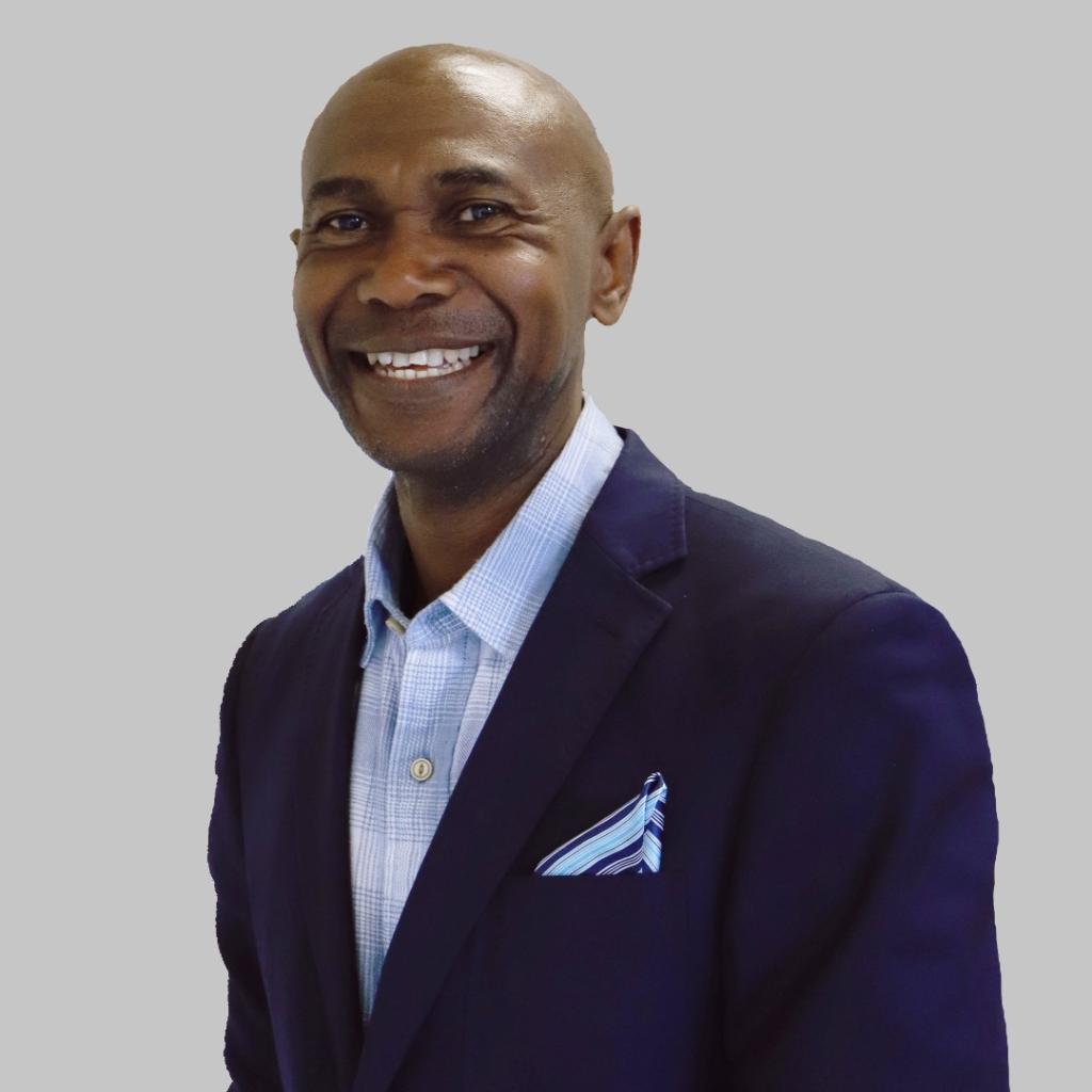 Olise Ogene smiling in front of a white background, wearing a suit.