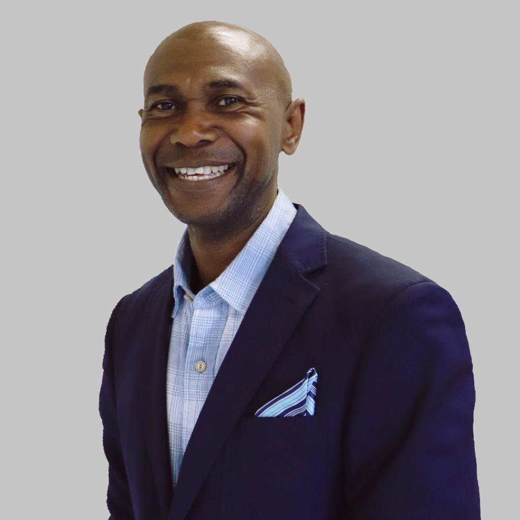 Olise Ogene smiling in front of a white background, wearing a suit. 