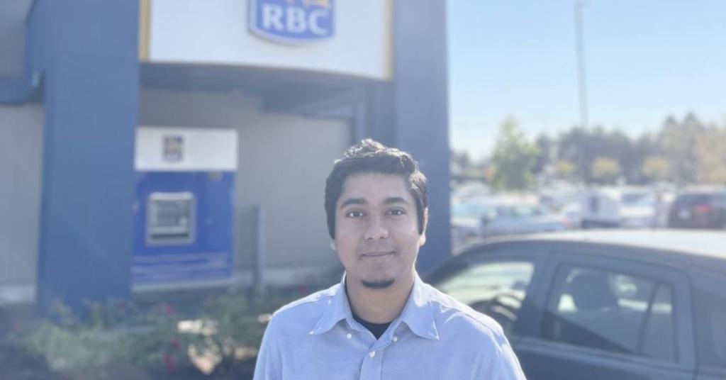 Photo of Ahamed Naveed Hasan wearing a blue shirt on a sunny day in front of a Royal Bank