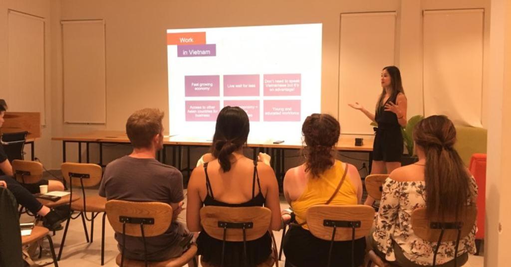 Vivian Trinh stands in front of an audience with a powerpoint presentation visible in the background