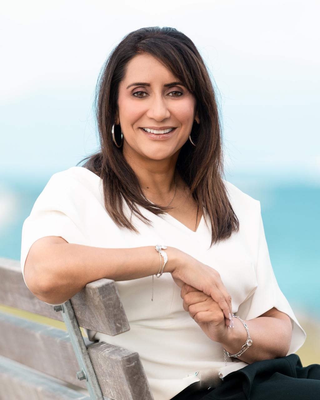 A woman smiles, looking at the camera while sitting off the side of a bench