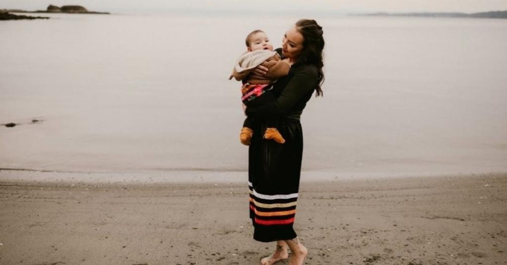 Tara Bouchard holding her baby, standing on a beach