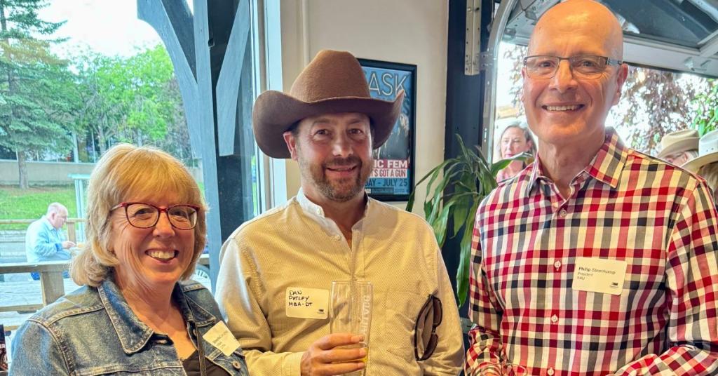Two alumni stand with the Royal Roads University president at an event