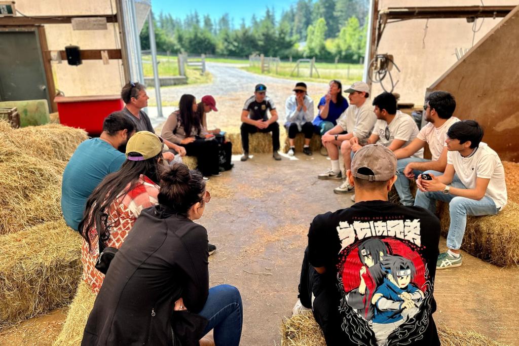 Students sit on hay bales in a pig barn