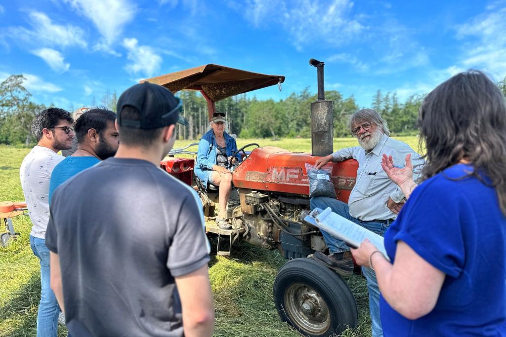 Students speak with sheep farmers around a tractor in a hay field