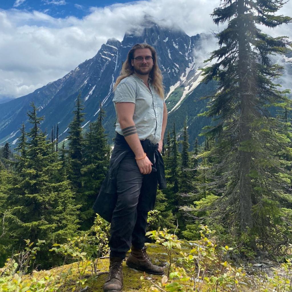 A man poses a top a forested mountain