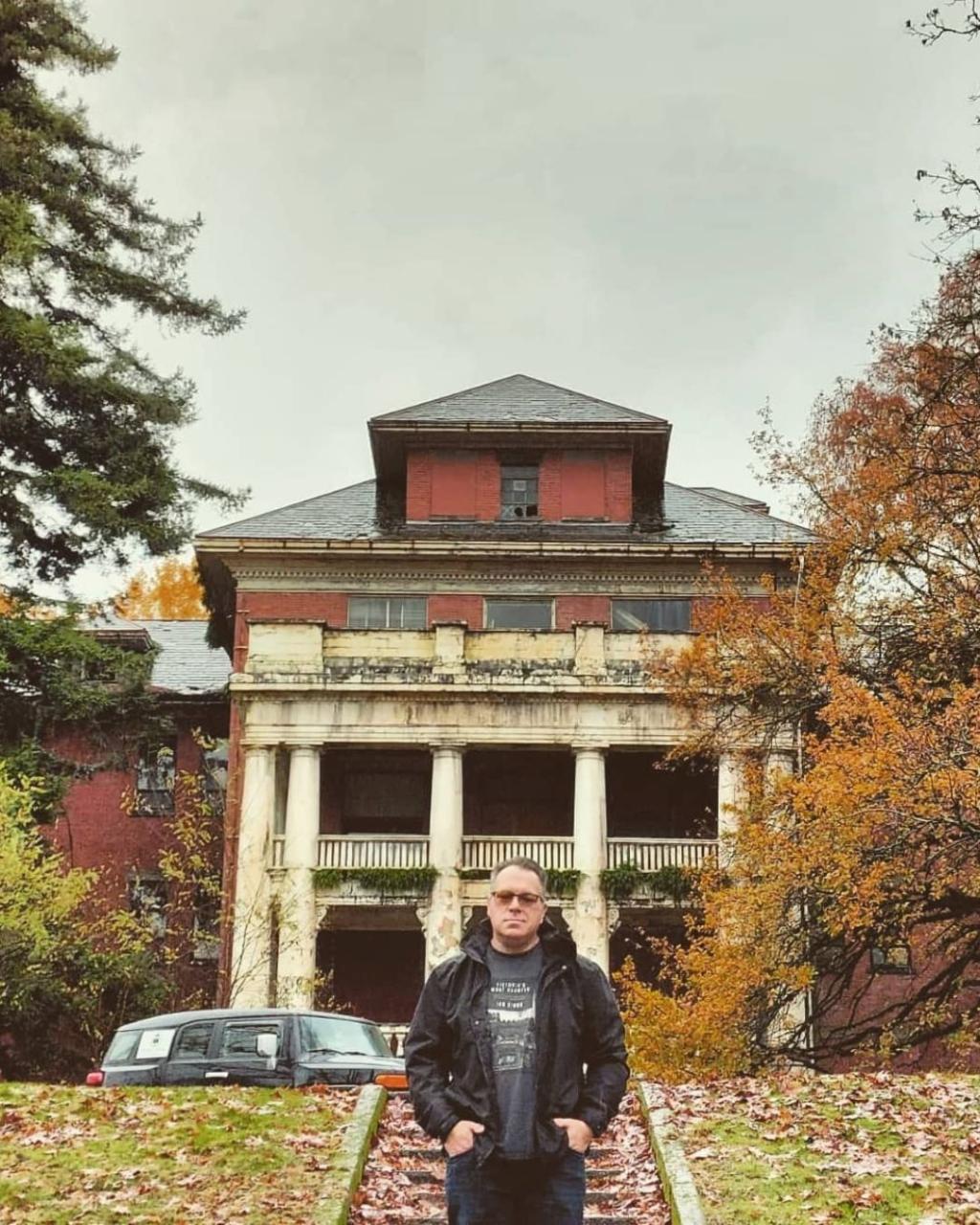 Ian Gibbs stands in front of an abandoned-looking old building