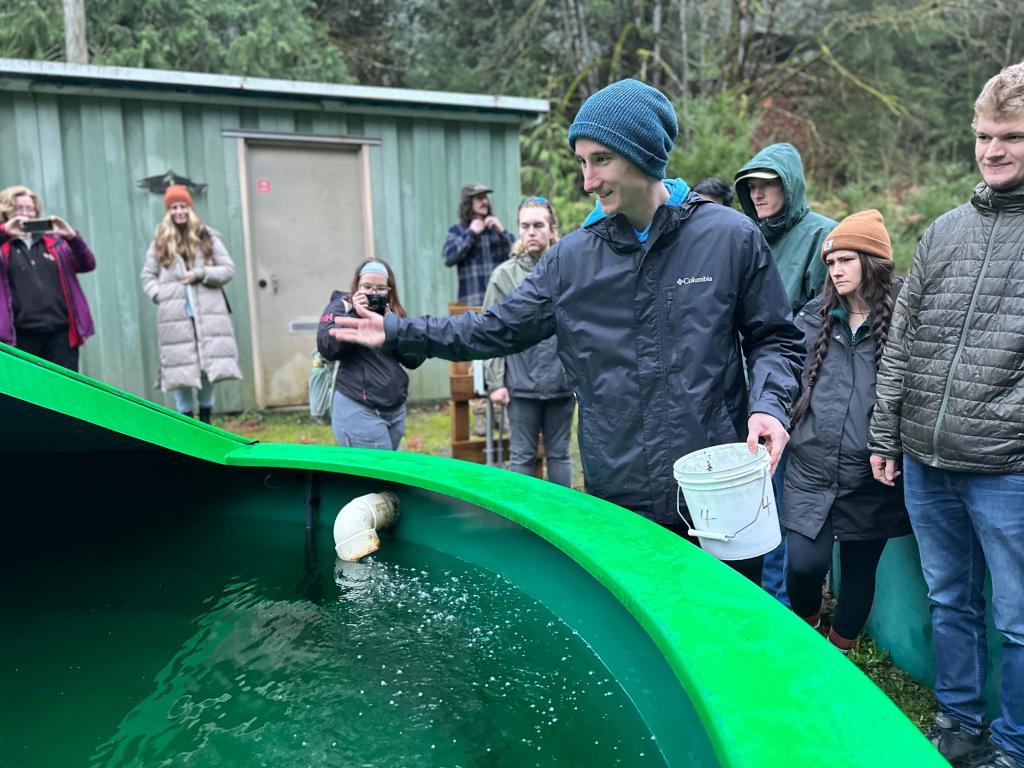 A student tosses food into a large fish tank