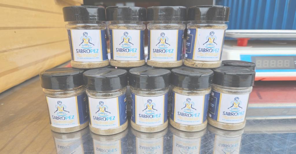 Jars of Sabropez fish powder stacked in two rows on a mirrored surface with a scale in the background.
