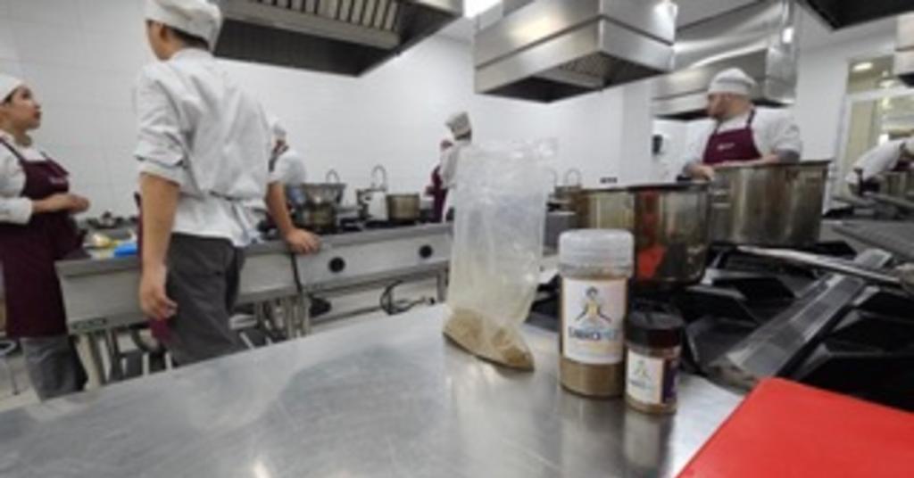 Commercial kitchen with two chefs talking in the background and a jar of Sabropez fish powder in the foreground.