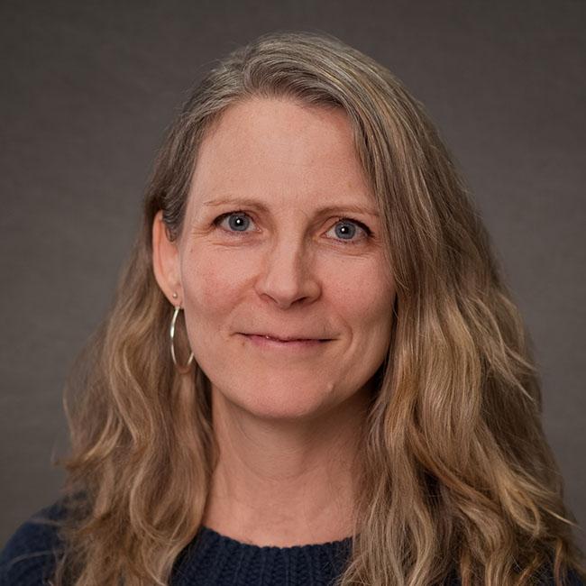 woman with shoulder length wavy blonde hair wearing a black sweater, slightly smiling