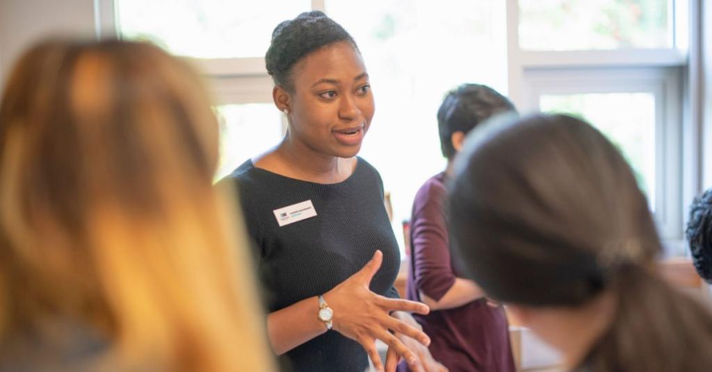 A woman gestures to students around an info booth