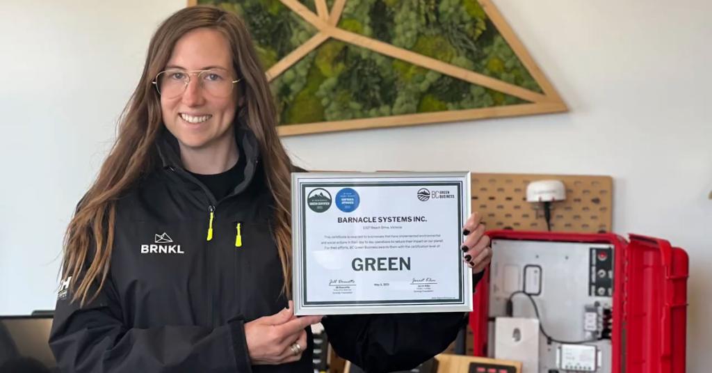 Mel Lacelle holding up certificate that says BC Green Business Barnacle Systems Inc.