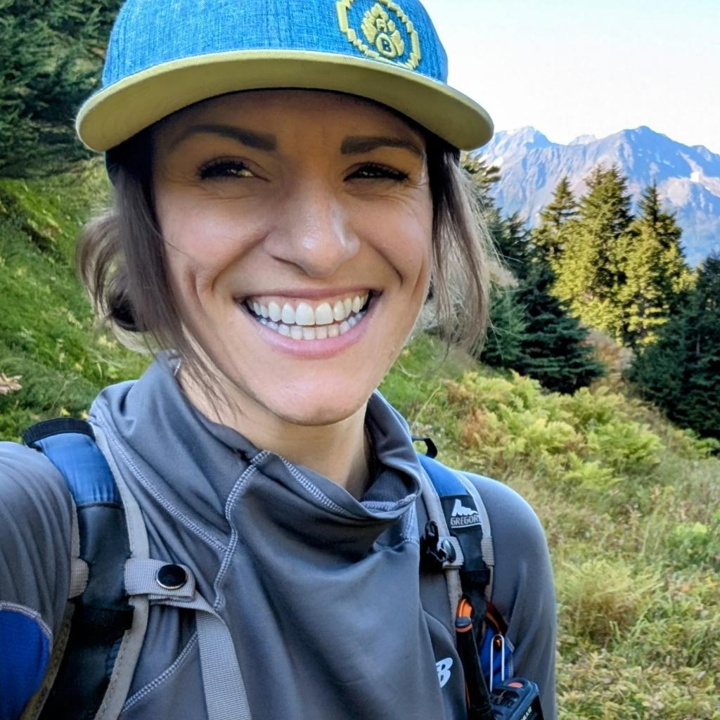 Chantelle Abma in the forested mountains, taking a selfie and grinning with a cool ball cap on.