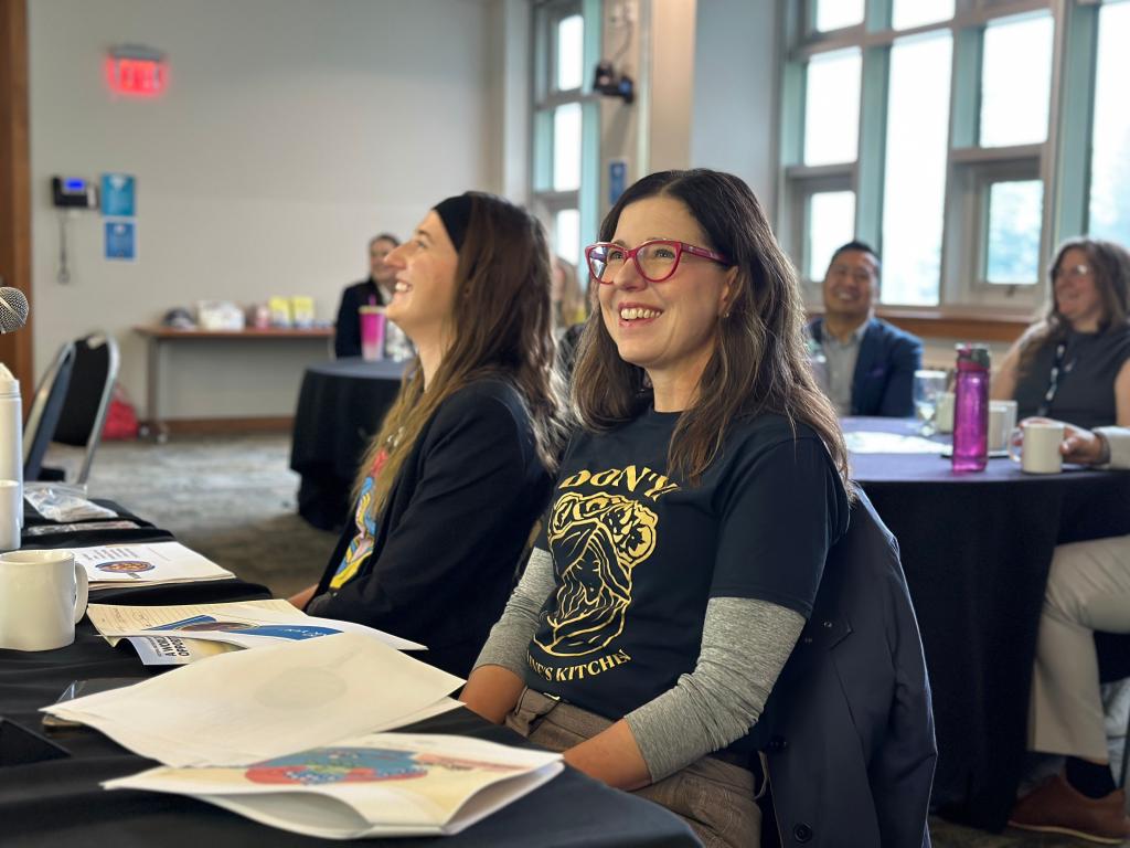 Two women sit at a table, smiling.