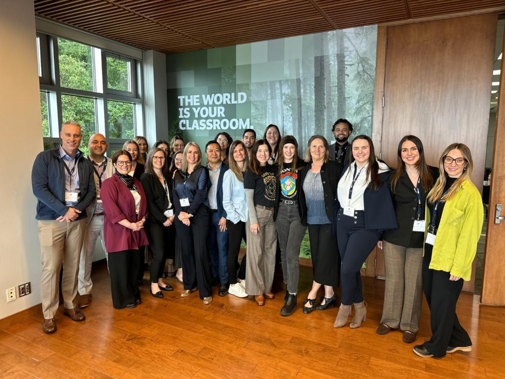 A group of MBAs pose for a photo. The words, "The world is your classroom" can be seen behind them.