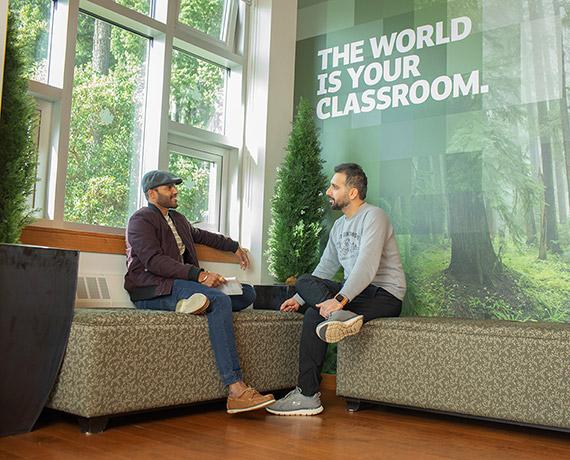 An RRU student sits in a lounge area and converses with an instructor next to a bright window