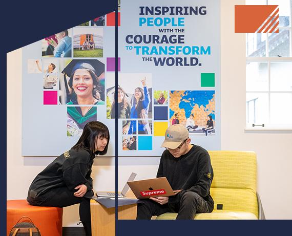 Two students sit and look toward a laptop in front of a poster in an RRU classroom.