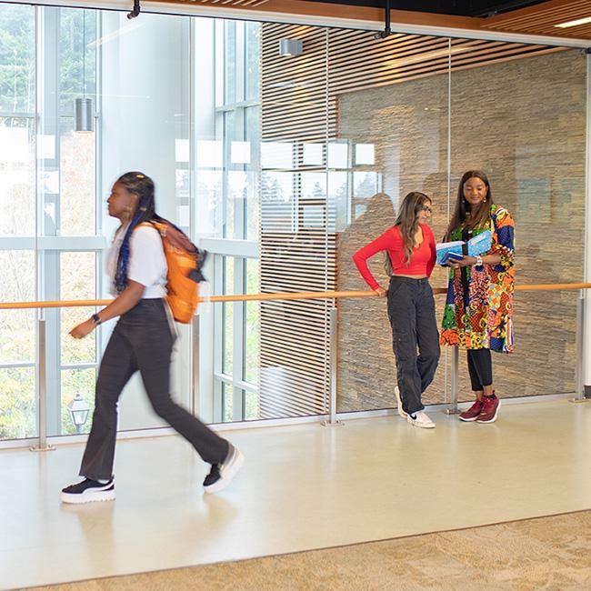 A student walks by two classmates leaning against a tall class wall in an RRU building