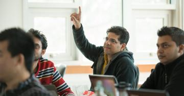 A student raises their hand in class with other students seated around them.