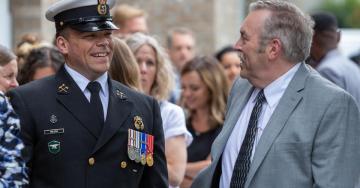 A person in military dress laughs with another person in front of a large group.