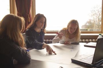 Students seated at a table in front of a window working on a project.