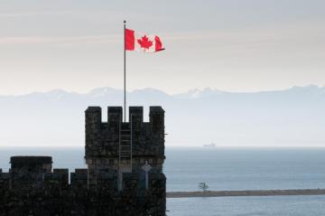 Canadian flag flying atop castle turret with ocean and mountains in the background.