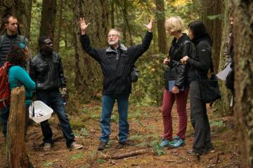 Group of people standing in a forest listening to an individual with raised arms.