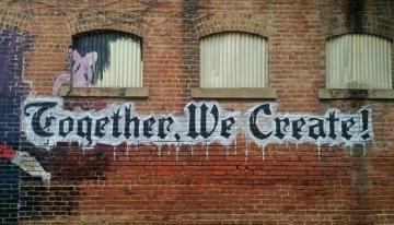 Words, "together, we create!" painted on side of brick building.