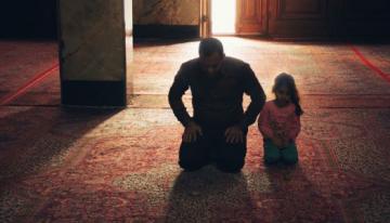 A child and adult kneeling in prayer.