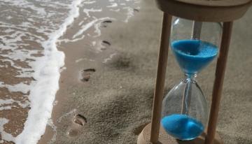 sand-timer-next-to-footprints-on-beach-and-ocean
