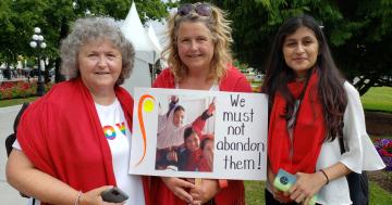 Three woman holding up a poster that reads, "We must not abandon them" at the Red Pashmina walk in July 2021.