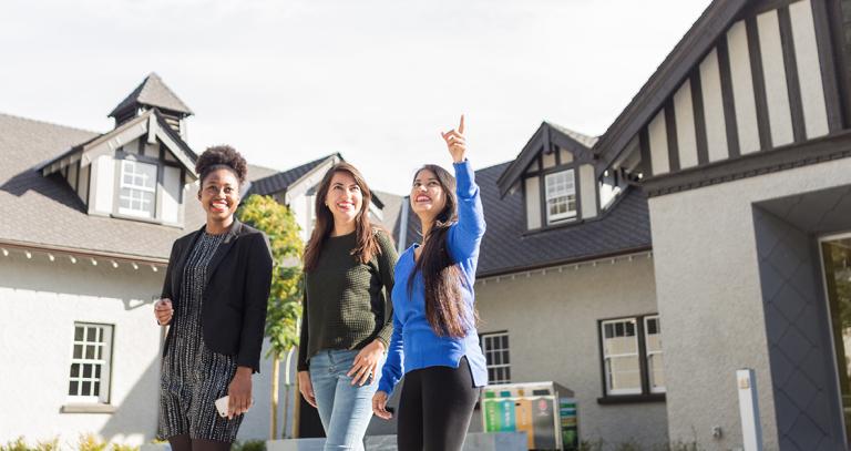 Three students in front of a building, pointing and looking at something