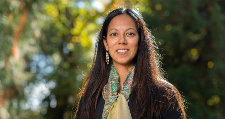 Dr. Runa Das standing in front of a forest backdrop