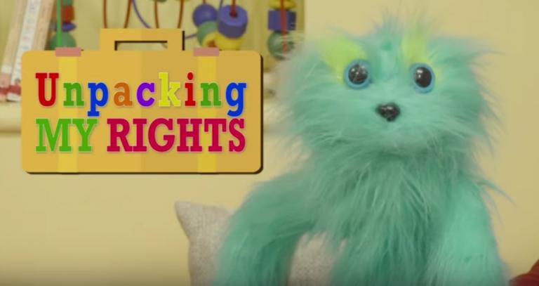 Still from video: turquoise fuzzy puppet beside sign saying "unpacking my rights"