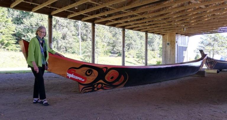 Prof. Leslie King standing next to a canoe under a wooden structure with a forested background.